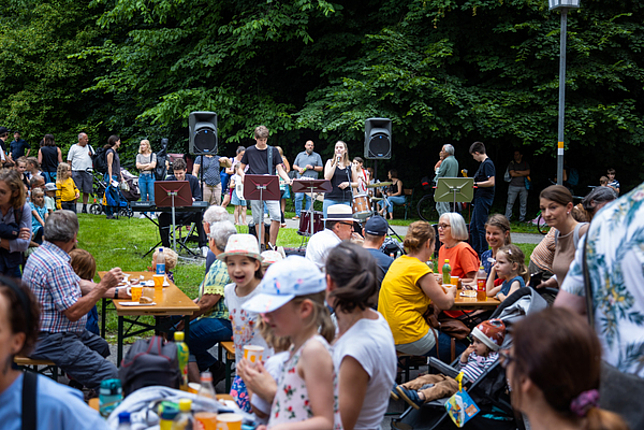 Viele Menschen sitzen im Reichenfeld an Tischen, im Hintergrund spielt eine Band. 