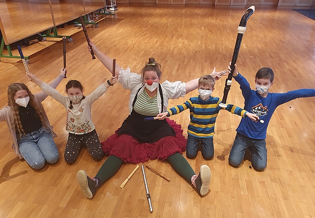 Clown Lililu, zwei Mädchen und zwei Jungen sitzen auf dem Boden und strecke die Arme in die Luft. 