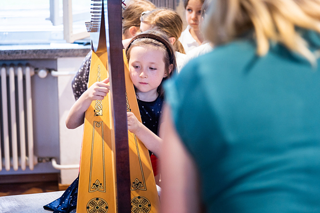 Ein kleines Mädchen spielt Harfe. 